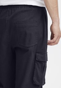 Pantaloni cargo negri cu talie elastică, dotati cu un buzunar posterior și un buzunar lateral pentru funcționalitate suplimentară. Textură netedă.