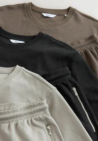 Tre afslappede sweatre i beige, sort og olivengrøn. Funktioner inkluderer standard crew neck, teksturerede striber og lynlåselementer.