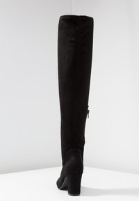 Bota negra por encima de la rodilla en suave material de ante, con un elegante silueta, tacón cuadrado y detalle de cremallera lateral.