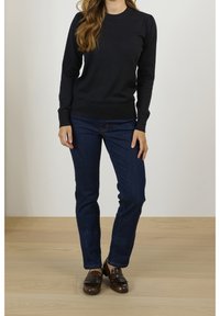 Maglione nero a maglia con maniche lunghe, polsini e orlo a costine, abbinato a jeans blu scuri e mocassini marroni. Design semplice e aderente.