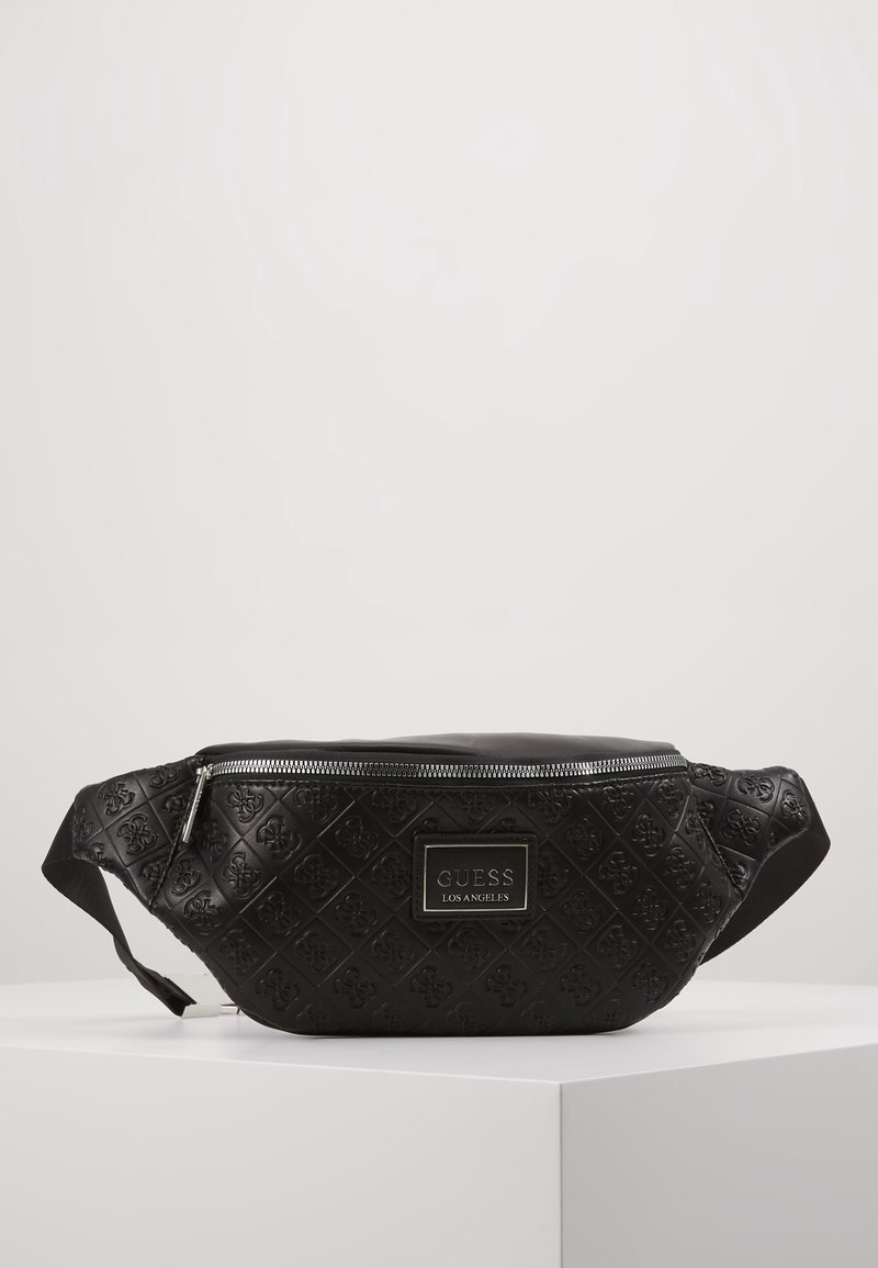 Sac banane noir Guess Los Angeles avec motif de logo embossé, fermeture éclair et sangle réglable, présenté sur un socle blanc.