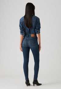 Mörkblå denim skinny jeans med hög midja, featuring en lädermärke, bakfickor, och kompletterad med en denimskjorta.
