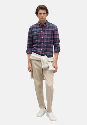 Karierter Hemd aus Baumwolle in Marineblau, Rot und Weiß, kombiniert mit beigen Hosen und weißen Sneakers; cremefarbener Pullover am Bauch gebunden.