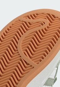 Podešev obuvi s vlnitým gumovým vzorem v oranžové barvě, s texturovaným bílým a šedým svrchním materiálem a kontrastními akcenty.