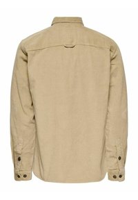 Beige Kordhemd mit langen Ärmeln, knöpfbaren Manschetten, Rückenpasse und einer kleinen Stoffschleife unter dem Kragen.