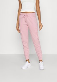 Ljusrosa sweatpants med elastisk midja, dragsko, sidofickor och ribbade avslut, tillverkade av mjukt tyg. Broderad logotyp på fickan.