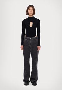 Schwarzer gerippter Bodysuit mit Ausschnitt und Perlenakzent, kombiniert mit verwaschenen schwarzen weit geschnittenen Jeans und klobigen schwarzen Schuhen.