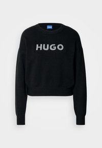 Zwart kort trui gemaakt van gebreide stof met het woord "HUGO" in zilver aan de voorkant, met lange mouwen en geribbelde manchetten.