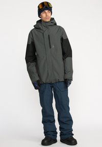 Gray and black hooded jacket with a zippered front, paired with blue snow pants. Equipped with gloves and skiing goggles.