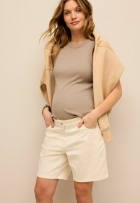 Beżowy prążkowany top na ramiączkach w połączeniu z kremowymi szortami, uzupełniony jasnobeżowym, oversize'owym hoodie zarzuconym na ramiona.
