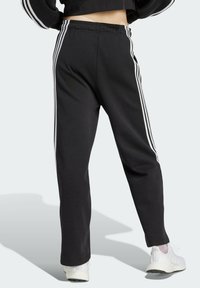 Schwarze Jogginghosen mit drei weißen Streifen an den Seiten, in normaler Passform und aus weichem Stoff. Kombiniert mit weißen Sportschuhen.