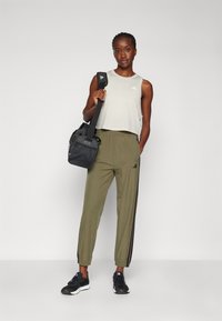 Lys grå avkortet tanktop og olivengrønne smale bukser med svarte sidestriper, kombinert med svarte joggesko og en svart treningsbag.