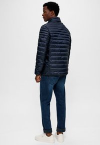 Navy puffer jacket met een hoge kraag, horizontale stiksels en logo-detail op de mouw. Gecombineerd met opgerolde spijkerbroek en witte sneakers.