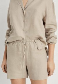 Beige linneskjorta med krage, knappstängning framtill och uppvikta ärmar; ihopparad med matchande shorts med elastisk midja och sidofickor.