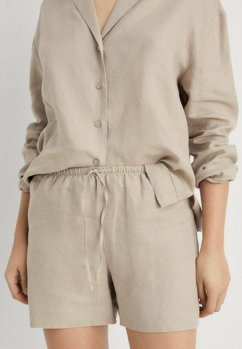 Beige linneskjorta med krage, knappstängning framtill och uppvikta ärmar; ihopparad med matchande shorts med elastisk midja och sidofickor.