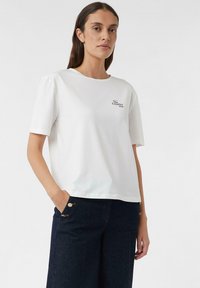Weißes Baumwoll-T-Shirt mit kurzen Ärmeln, rundem Ausschnitt und einem kleinen schwarzen "We Creative" Schriftzug auf der Brust.