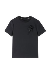 Camiseta de algodón negra con mangas cortas y cuello redondo, que presenta una decoración floral en 3D con acentos de cuentas en el lado izquierdo del frente.