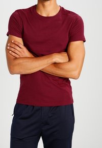 Camiseta de manga corta burdeos en un diseño ajustado, hecha de un material suave; presenta una textura lisa con un cuello redondo clásico.