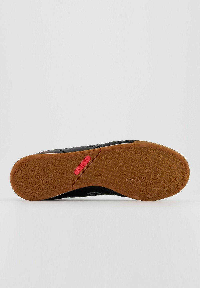 Sneaker noir avec une semelle en caoutchouc texturée, présentant des motifs circulaires et un accent rose sur le côté. Matériau supérieur durable avec une finition lisse.
