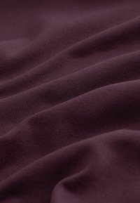 Gros plan sur un tissu doux et texturé de couleur violet profond, avec de légers plis et un motif tissé subtil.