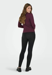Burgunderfarbener Langarm-Oberteil kombiniert mit schwarzen Skinny-Jeans. Das Oberteil hat ein schlichtes Design; die Jeans verfügen über einen klassischen Fünf-Taschen-Stil und dezente Nähte.