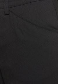 Mustat housut, jotka on valmistettu teksturoidusta kankaasta, jossa on kirkas pinta. Housuissa on piilotettu sauma-asia ja viistotaskut.