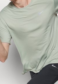 Světle zelené sportovní tričko s krátkým rukávem, kulatým výstřihem a malým stříbrným logem Nike na hrudi. Hladký povrch látky.