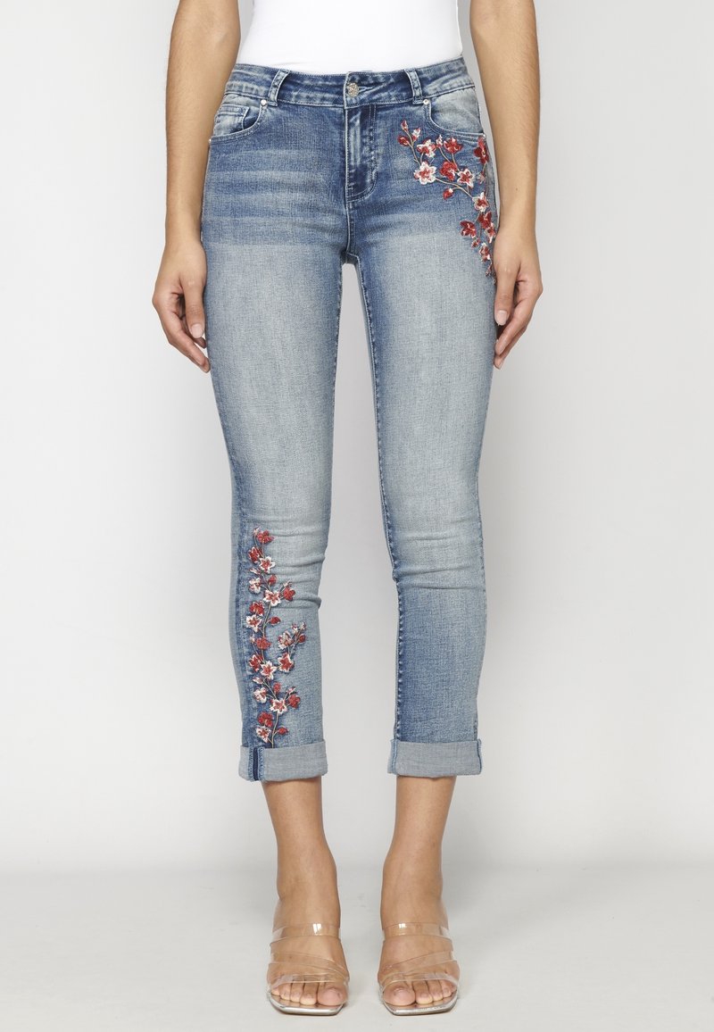 Hellblaue Denim-Jeans mit floralen Stickereien in Rot und Weiß am linken Bein, schlank geschnitten mit hochgekrempelten Säumen am Knöchel.