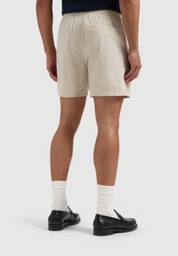 Katoenen, lichtbeige shorts van een gestructureerde stof; elastische tailleband; enkele achterzak; gecombineerd met witte sokken en zwarte instapschoenen.
