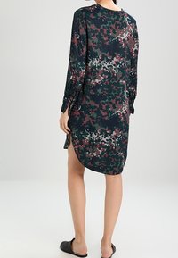 Vestido de manga larga en verde oscuro con un patrón de camuflaje en tonos burdeos y gris. Presenta un escote redondo y aberturas laterales.