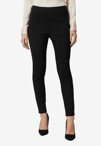 Černé kalhoty na míru se slim fit střihem, vyrobené z elastického materiálu. Mají hladký povrch a střední pas. Žádné viditelné kovové prvky.