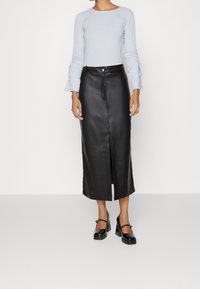 Lång svart läderkjol med en framficka, ihopparad med en ljusblå ribbad långärmad topp med samlade bjälkar. Svarta platåskor.