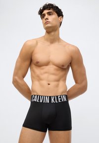 Black stretch boxer briefs with a wide black waistband featuring white "CALVIN KLEIN" logo; smooth texture; fitted design.