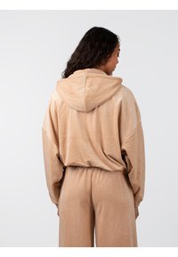 Sudadera oversized beige con un acabado texturizado, que presenta una capucha con cordón y una cintura elástica, combinada con pantalones a juego.