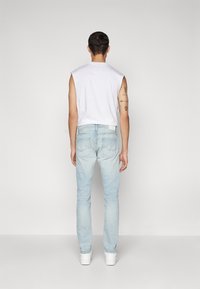 Åtsittande vit ärmlös topp, ljusblå raka jeans och vita sneakers, sedd bakifrån mot en neutral grå bakgrund.