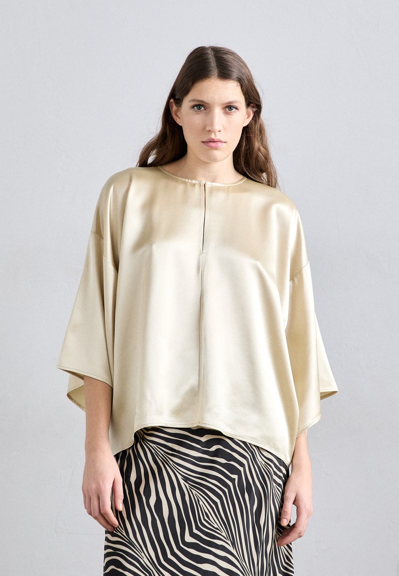 Satin, lichtbeige top met een hoge halslijn en brede mouwen, gecombineerd met een zwart en crèmekleurige gestreepte rok met een vloeiend ontwerp.
