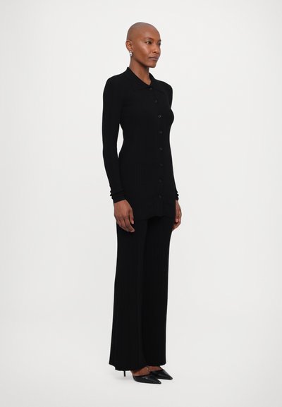 Černý žebrovaný kardigan s dlouhými rukávy, knoflíkovým zapínáním vpředu, spárovaný s odpovídajícími širokými kalhotami a špičatými černými podpatky.