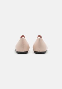Ballerine in pelle nuda con punta arrotondata, design minimalista, dettaglio del tallone rosa a contrasto e sottile suola nera. Vista posteriore.