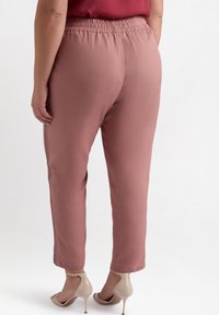 Różowe, lekkie spodnie z elastycznym paskiem, zwężającym się krojem nogawek, bocznymi szwami i gładką fakturą. Noszone z cielistymi szpilkami.