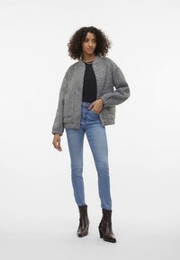 Grijs gestructureerd oversized jack met drukknoopsluiting, zwarte top, lichtblauwe skinny jeans en bruine enkellaarsjes met hak.