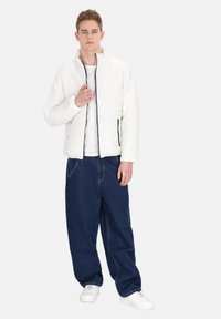 Jachetă albă matlasată cu guler înalt, fermoar negru; asortată cu pantaloni largi din denim albastru și adidași albi. Design simplu și croială lejeră.