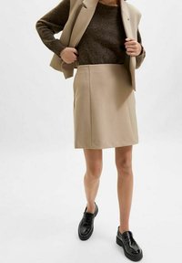 Beige kjol i slät tygkvalitet, knälång, i kombination med en brun tröja och en beige kavaj. Svarta skor med platåsål.