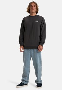Mørkegrå bomulds-sweatshirt med rund halsudskæring, ribbede manchetter og kant. Har et lille hvidt logo på brystet. Bæres med lyseblå bukser.