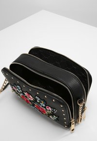 Borsa a tracolla in finta pelle nera con ricamo floreale, borchie dorate, doppio scomparto con zip e una tracolla a catena per la versatilità.