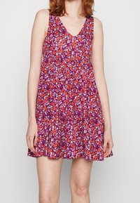Květinové šaty v purpurových a červených odstínech, bez rukávů s výstřihem do V, lehký materiál, rozšířený střih, s nařaseným pasem a vzorovaným designem.