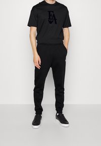 Svart bomullströja med en logo och matchande svarta sweatpants. Outfitten har en avslappnad passform och elastisk midja, och kompletteras med svarta sneakers.