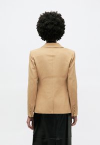 Ταμπά σακάκι με μία σχισμή, πέτα γιακά και τέσσερα κουμπιά στα μανίκια, συνδυασμένο με μαύρη δερμάτινη φούστα.