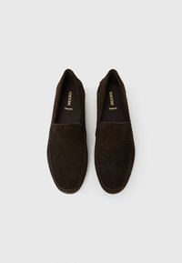 Σκούρα καφέ σουέντ μοκασίνια Geox Respira slip-on με ορατή ραφή, επίπεδη σόλα και στρογγυλεμένη μύτη, σε λευκό φόντο.