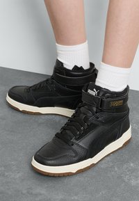 Czarne wysokie sneakersy z cholewą skórzaną i syntetyczną, z białą podeszwą pośrednią i gumową podeszwą zewnętrzną. Teksturowane akcenty i detal z logo.