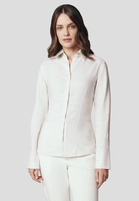 Biała, długa koszula z długim rękawem i zapięciem na guziki, wykonana z teksturowanej tkaniny; posiada dopasowany krój i mankiety.